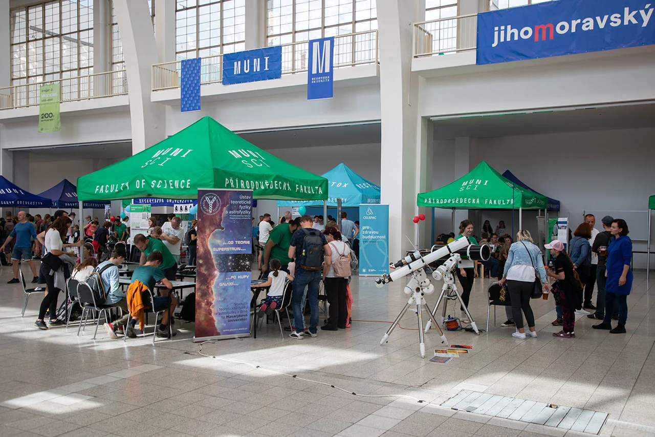 Návštěvníci mezi zelenými stánky Masarykovy univerzity v hale Festivalu vědy