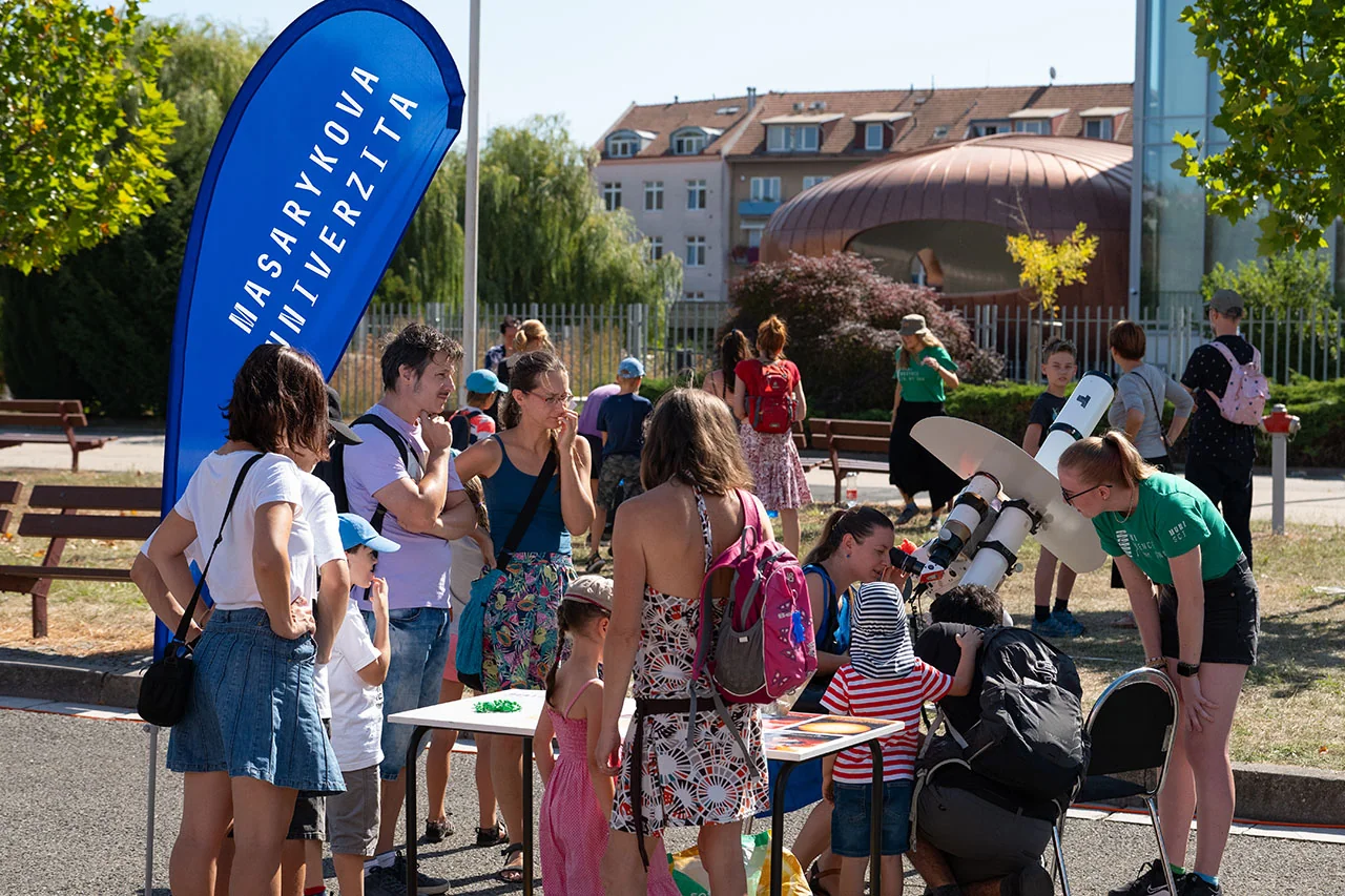 Rodiny u venkovního stánku s vlajkou Masarykovy univerzity